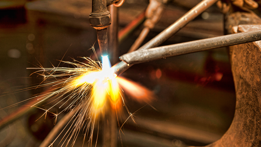 Close-up of a welder cutting metal, with bright sparks and glowing flame in a workshop