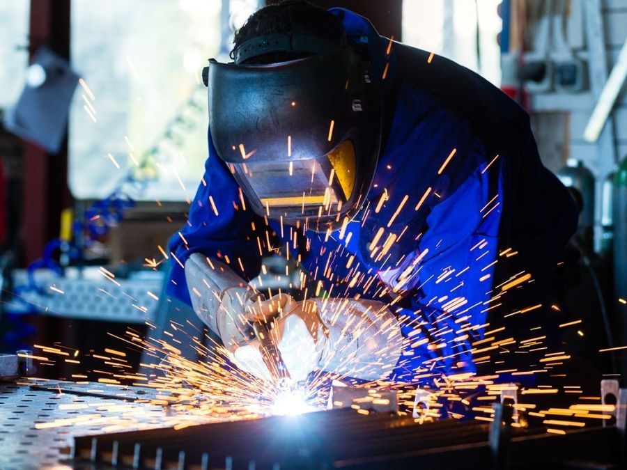Welder in a blue jacket and helmet creating bright sparks while welding metal indoors