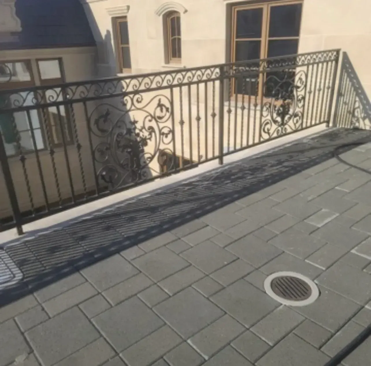 Rooftop terrace with gray pavers, ornate black railing, and cream building windows.