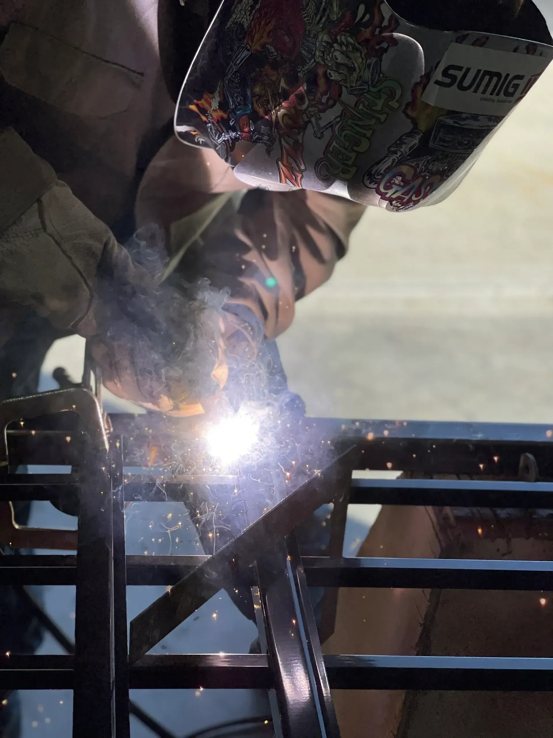 Person welding metal on a frame, with bright sparks and a protective helmet.