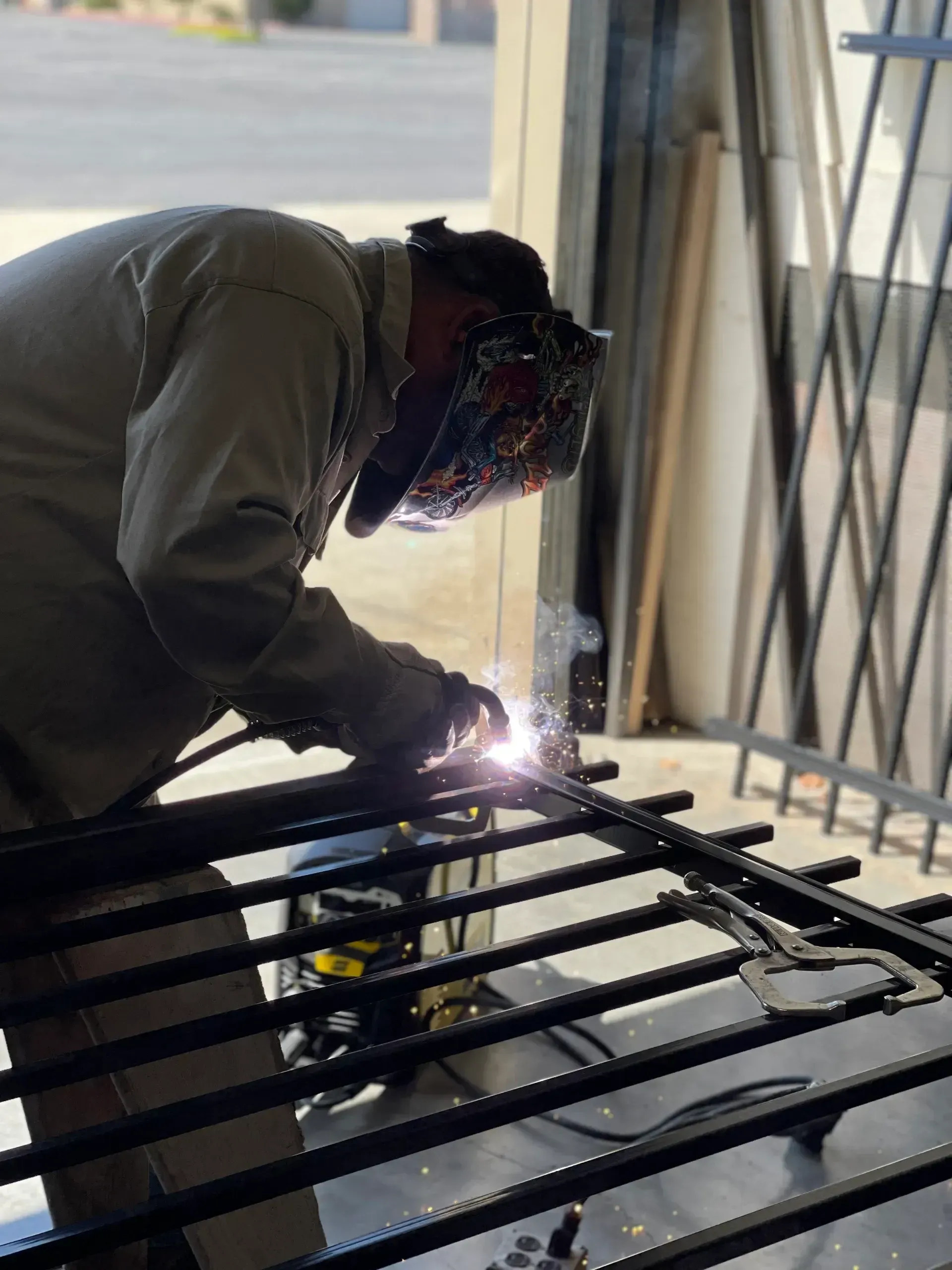 Welder in protective gear welding a metal frame indoors, bright sparks visible.