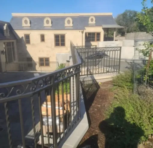 Sunny view of a beige apartment building with black wrought-iron railings and a small garden path