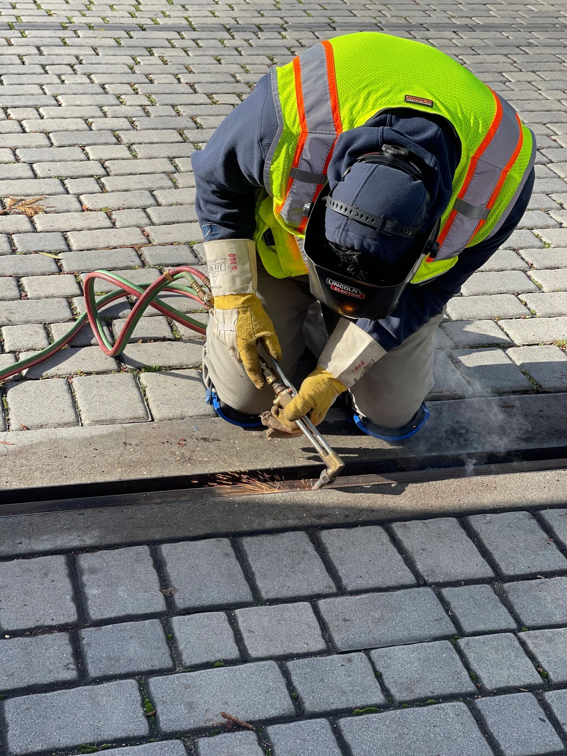 Worker in a high-visibility vest repairing cobblestone pavement with tools.