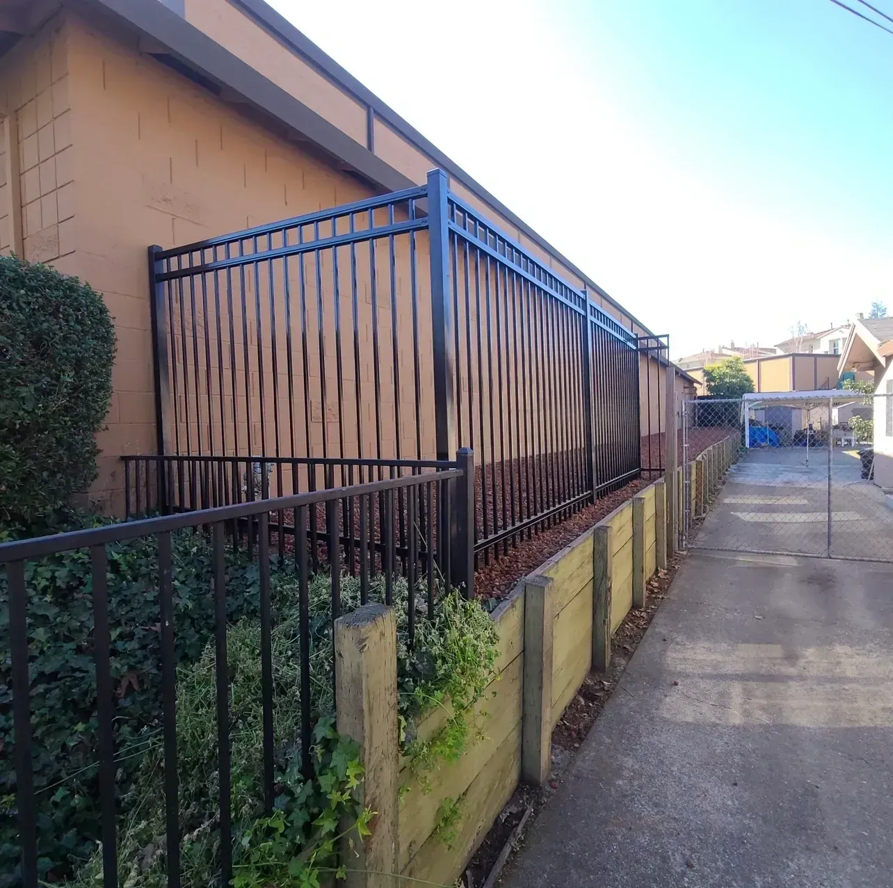 Narrow alley beside a tan house with a black metal fence and yellow retaining wall