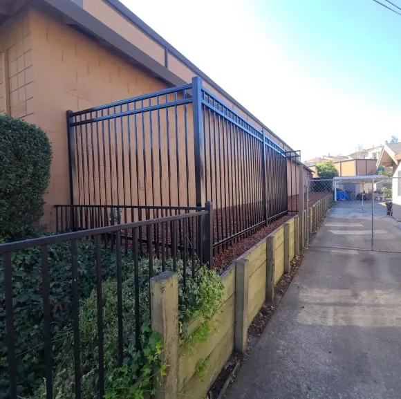 Narrow alley beside a tan house with a black metal fence and yellow retaining wall