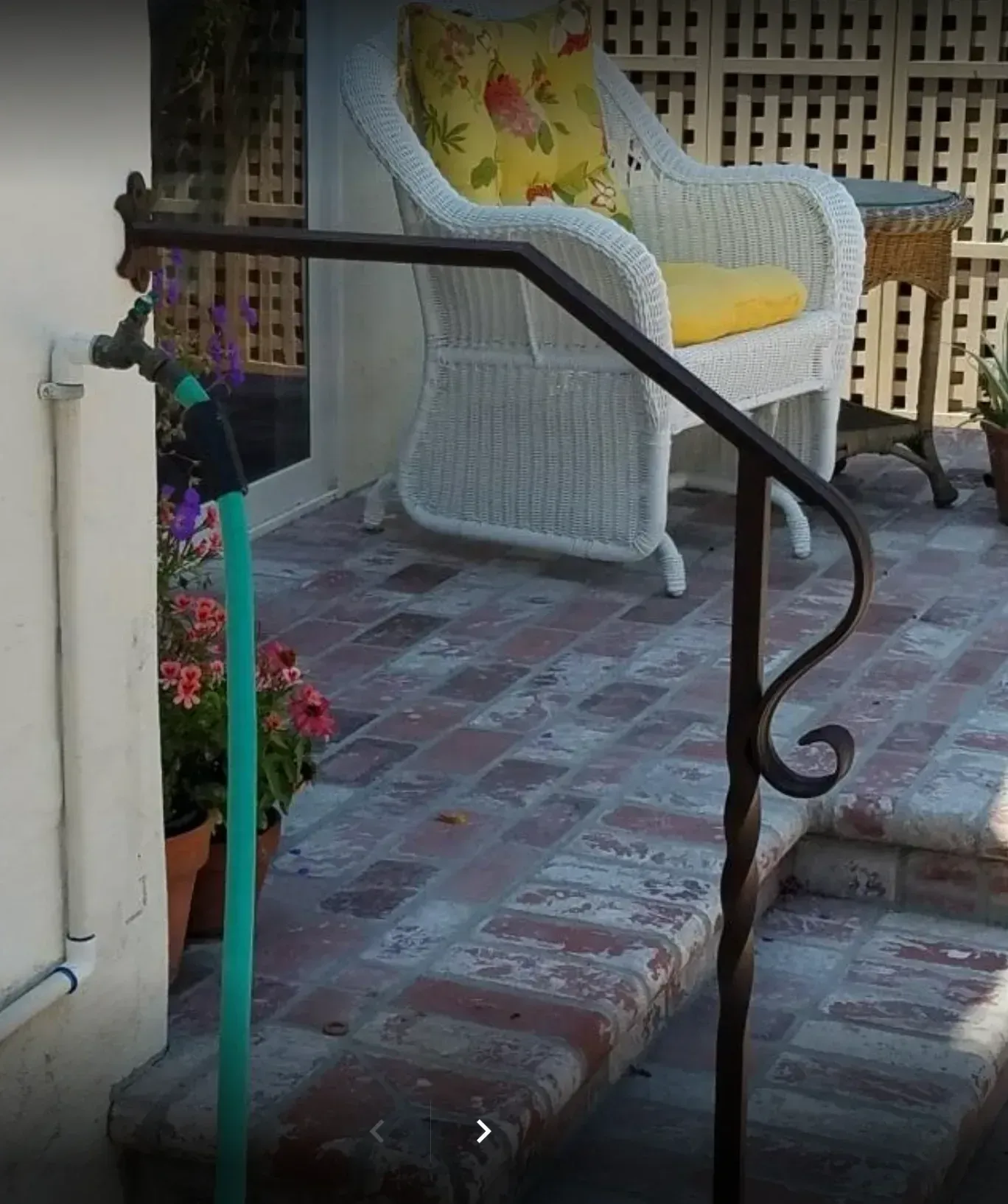 Brick patio steps with a black handrail and a white wicker chair with yellow cushion on the porch