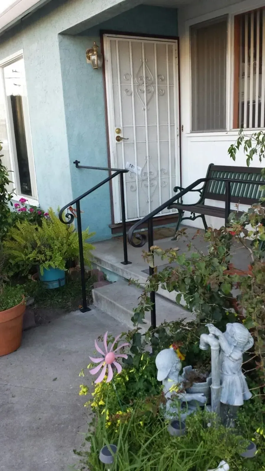 Front porch with blue stucco wall, white security door, black bench, potted plants, and a concrete walkway.
