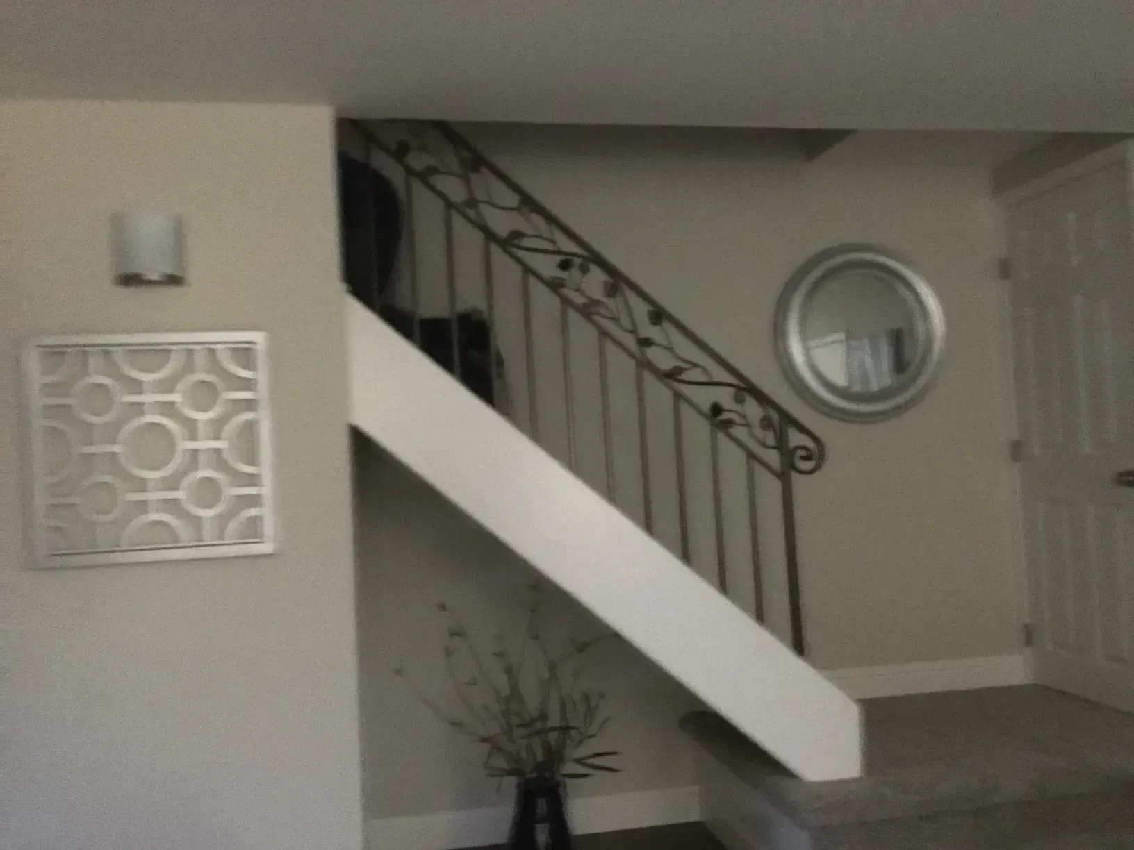 Interior staircase with white railing, circular mirror, and wall decor in a beige entryway