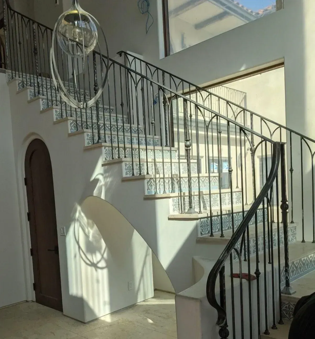 Sunlit indoor staircase with black railings and tiled steps in a white entry hall