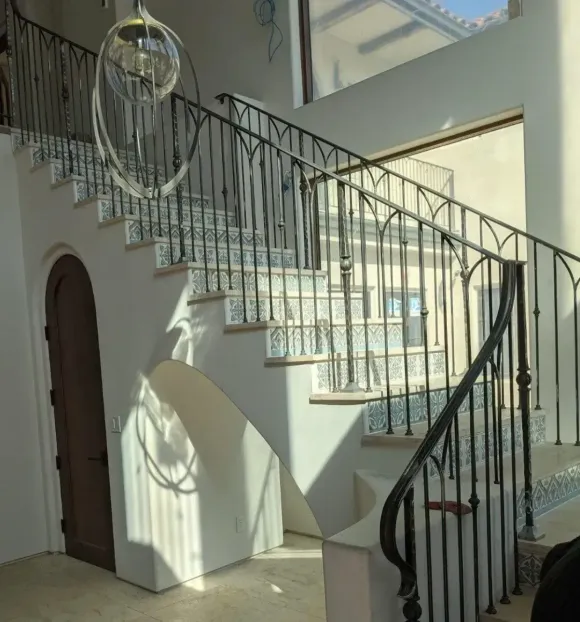 Sunlit indoor staircase with black railings and tiled steps in a white entry hall