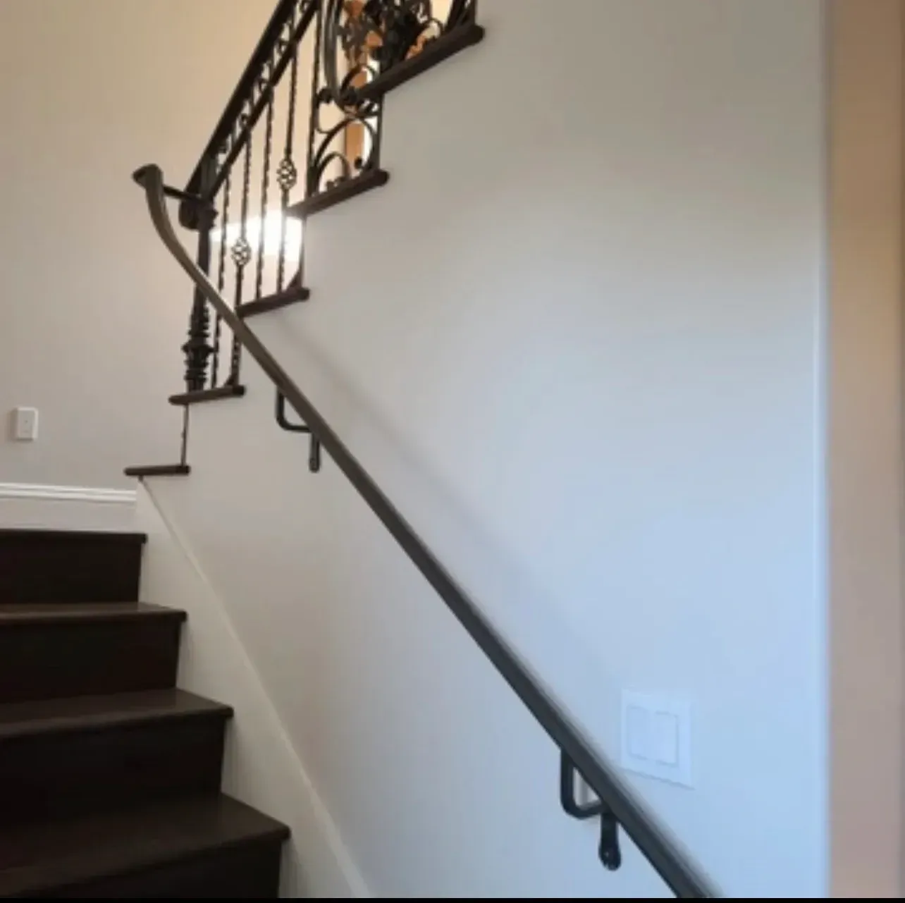 Indoor staircase with dark wood steps, white walls, and a decorative black iron railing