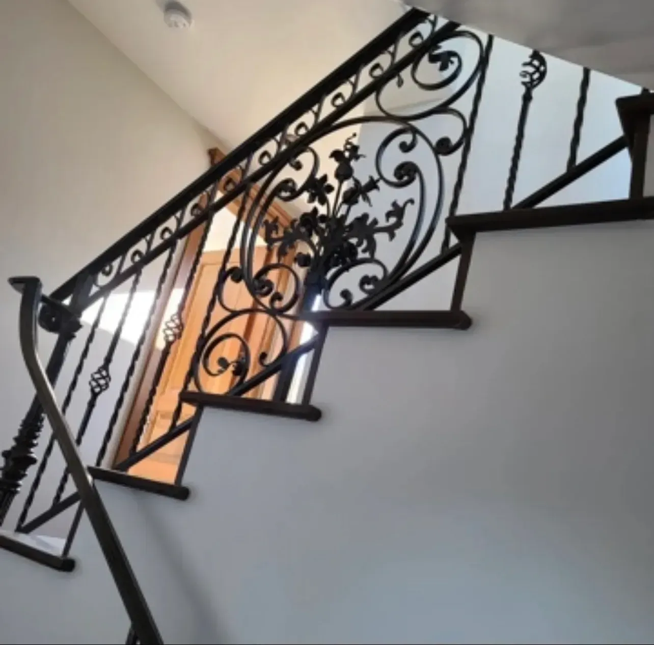 Ornate black wrought-iron staircase railing against white walls in a bright interior