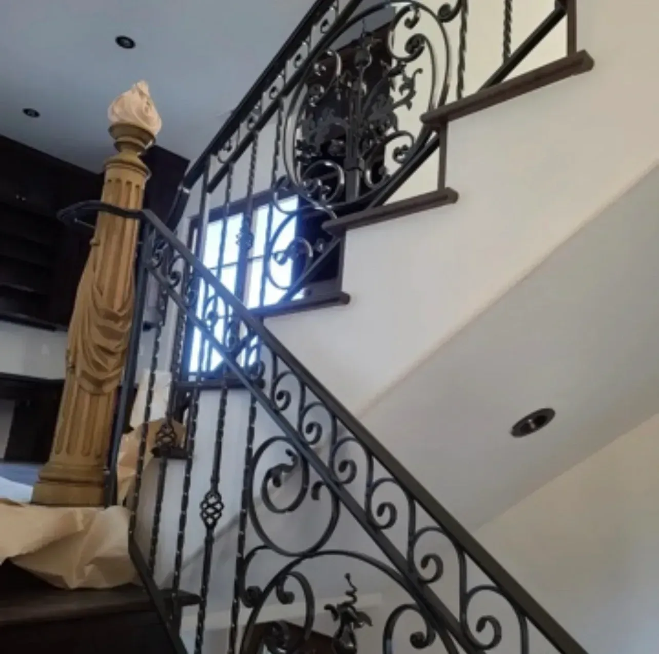 Ornate black metal staircase railing beside a white wall and window in a home interior