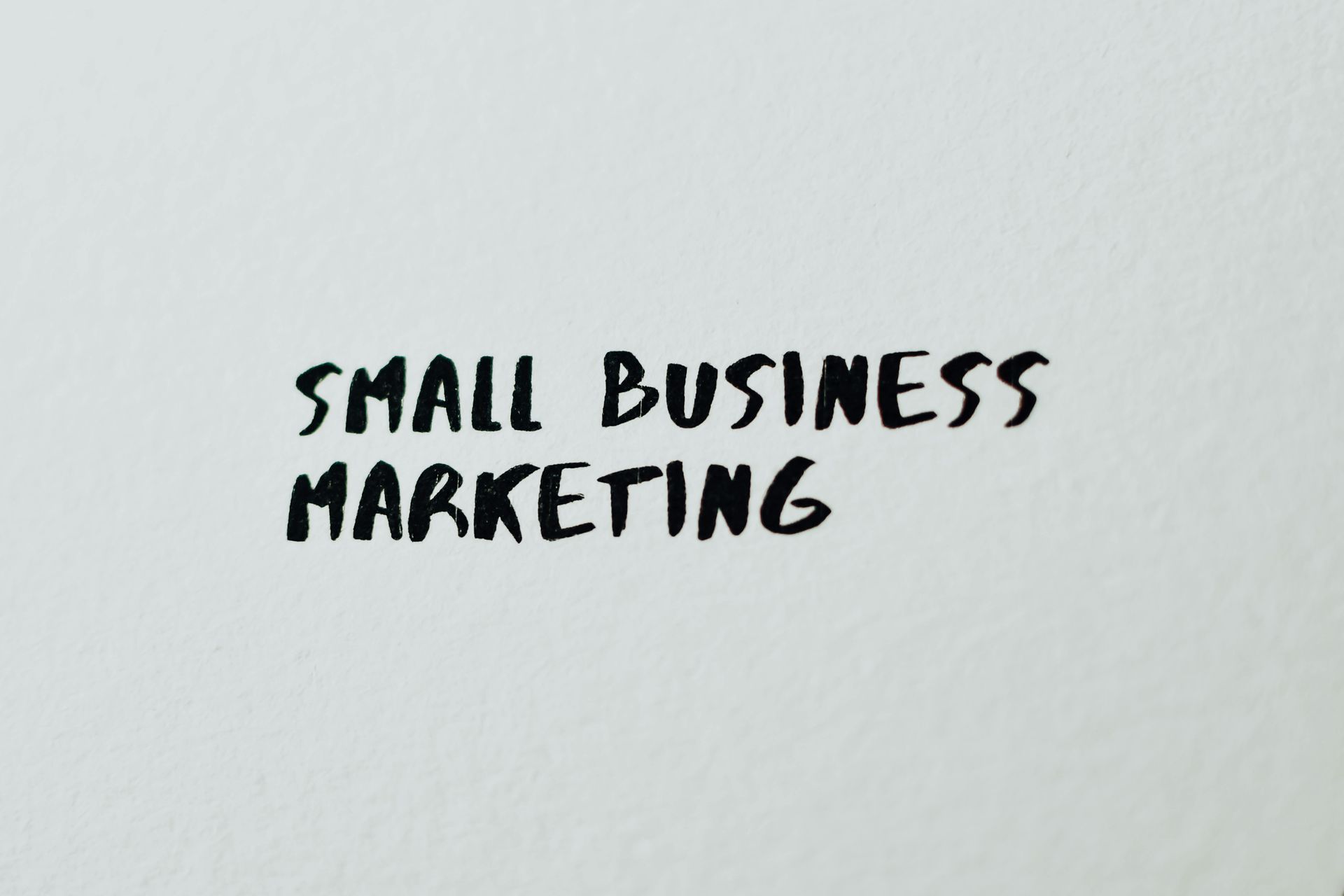 Black handwritten text on white paper reading “SMALL BUSINESS MARKETING”