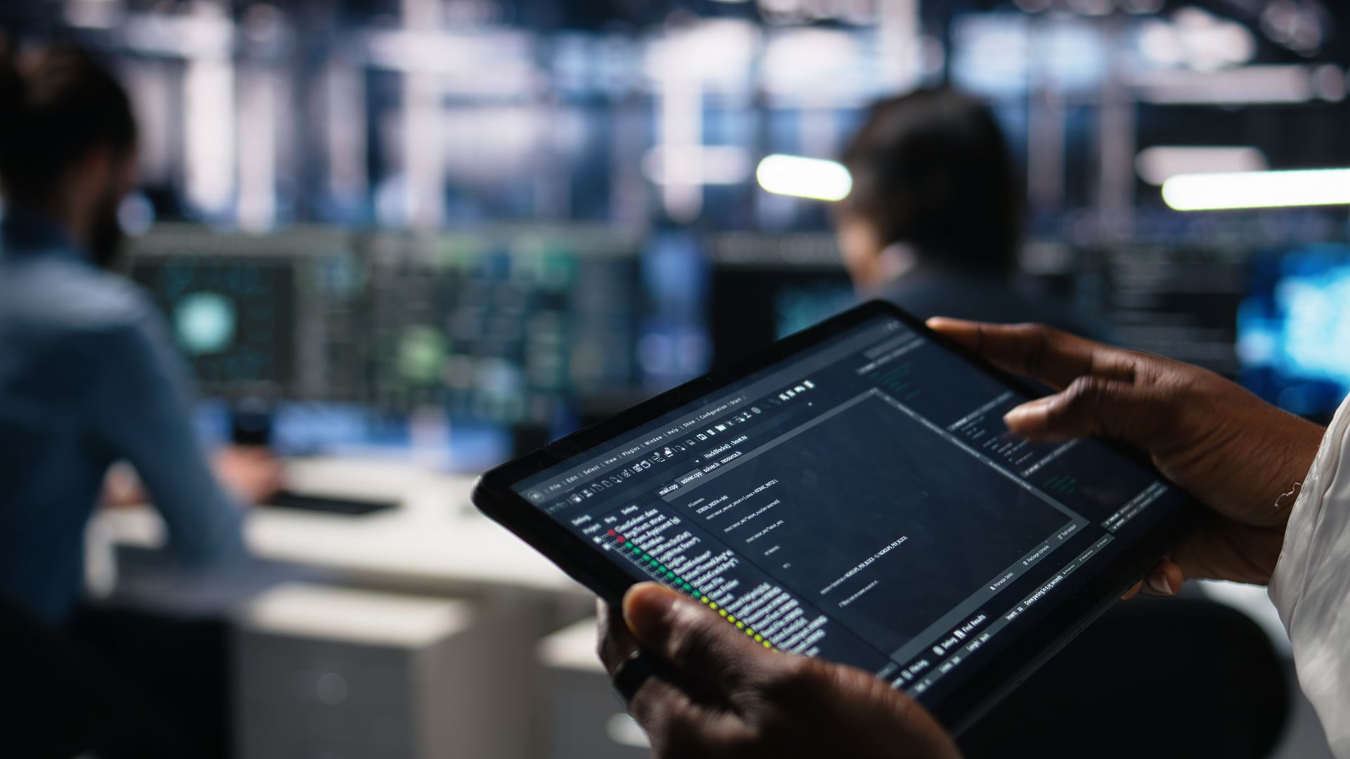 Close-up of data center software developer using a tablet to review code at a server hub.