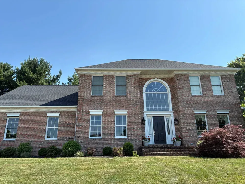 Two-story brick house with a dark roof and large arched front windows under a bright blue sky.