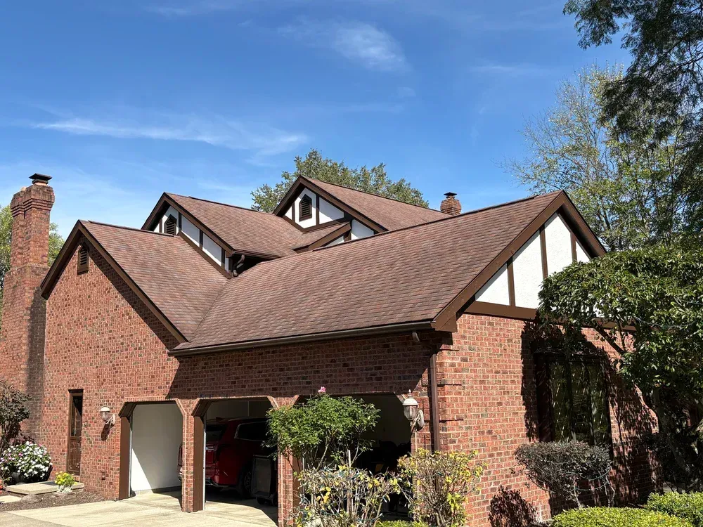 Brick house with brown roof, white trim, and a clear blue sky.