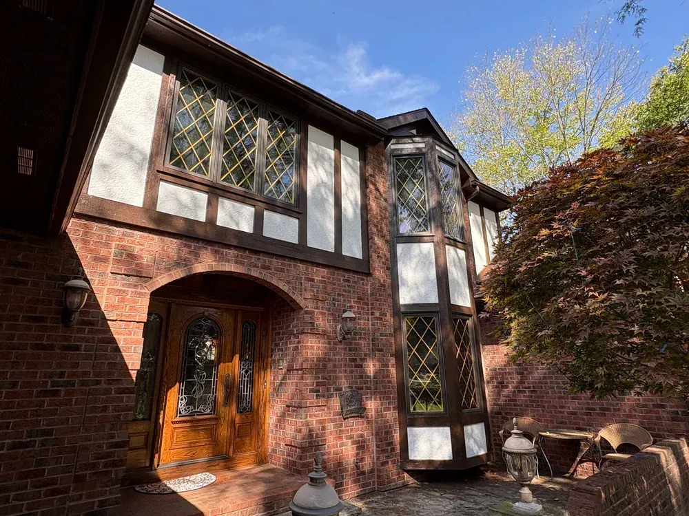Brick Tudor-style house with dark brown trim, white accents, and arched doorway, under a blue sky.