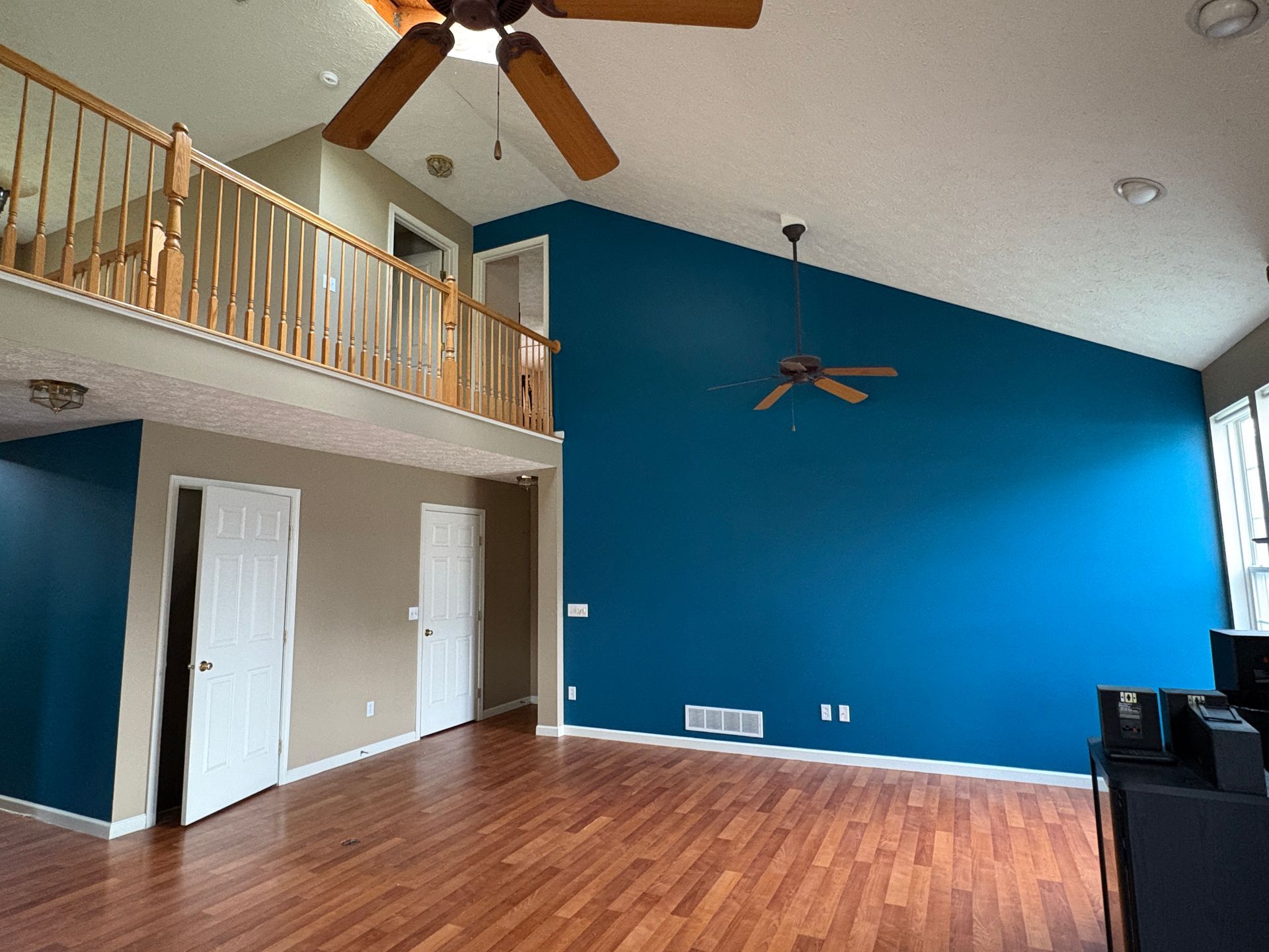 Spacious living room with blue accent wall, loft, hardwood floors, and ceiling fans.