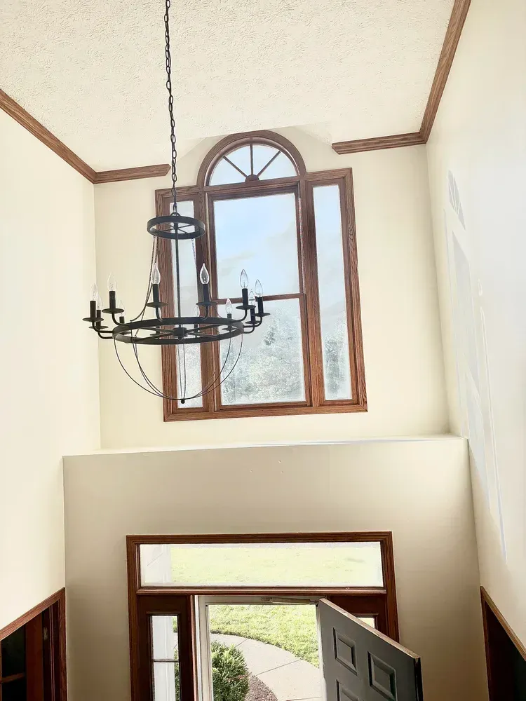 High-ceilinged entry with arched window, chandelier, and a front door. Cream walls, brown trim.