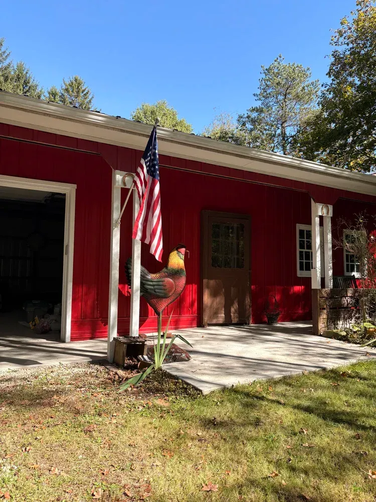 Red barn with an American flag and rooster statue in front.