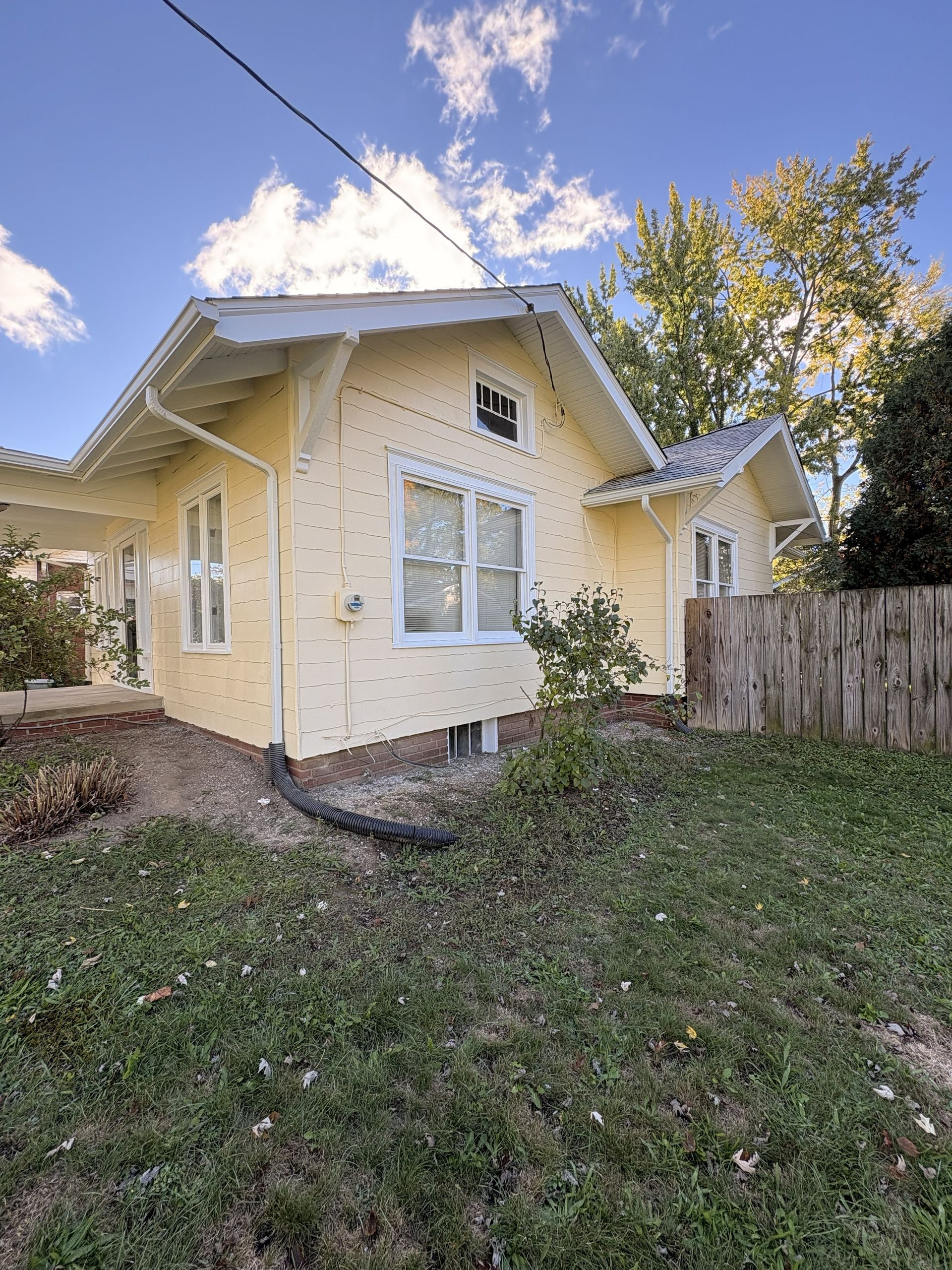 Yellow house with white trim, set under a blue sky. A wooden fence is in the background.
