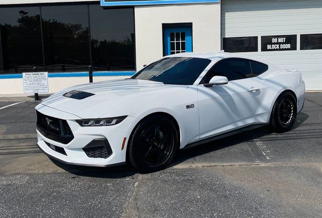 A white ford mustang is parked in front of a garage.