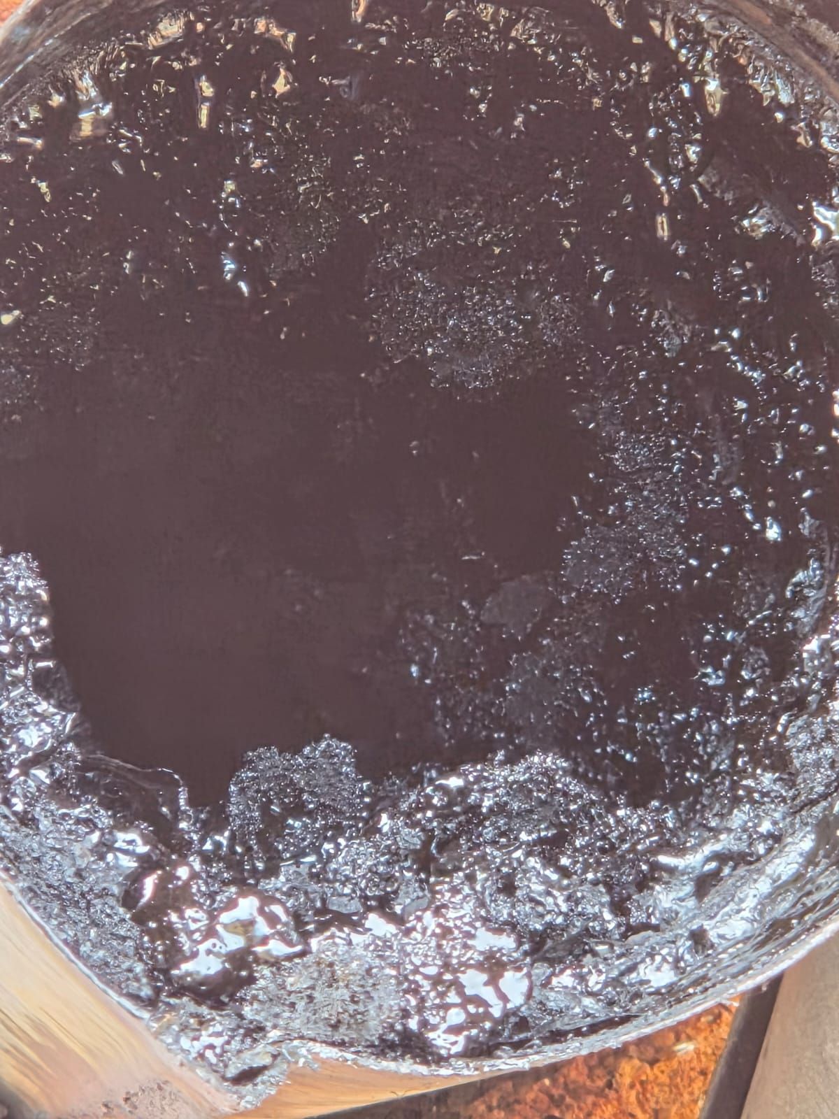 Primo piano di un contenitore pieno di un liquido denso, scuro e lucido, probabilmente olio.