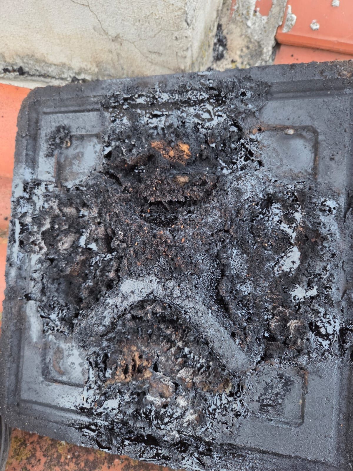 Contenitore di plastica nera fusa e fortemente carbonizzato. Tracce di un incendio con detriti.