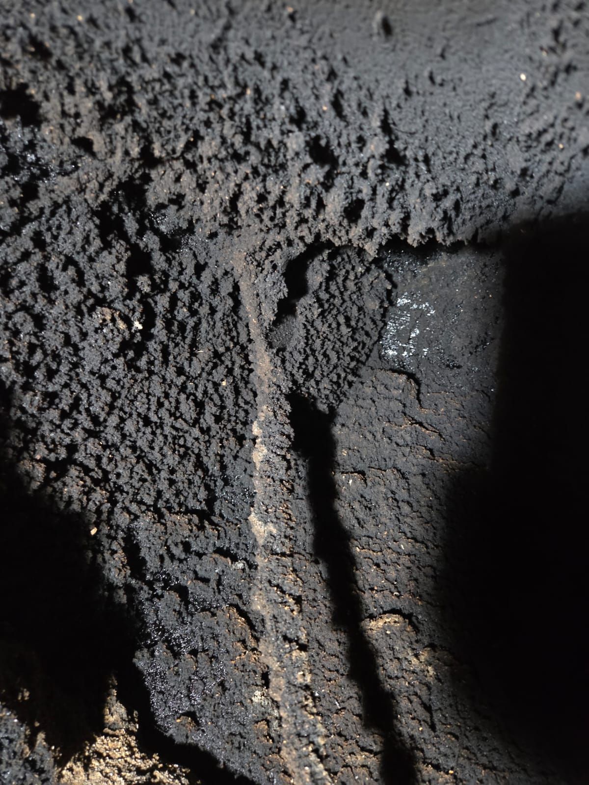 Primo piano dell'interno di un camino scuro e fuligginoso. Accumuli di creosoto nero ricoprono le pareti di mattoni.