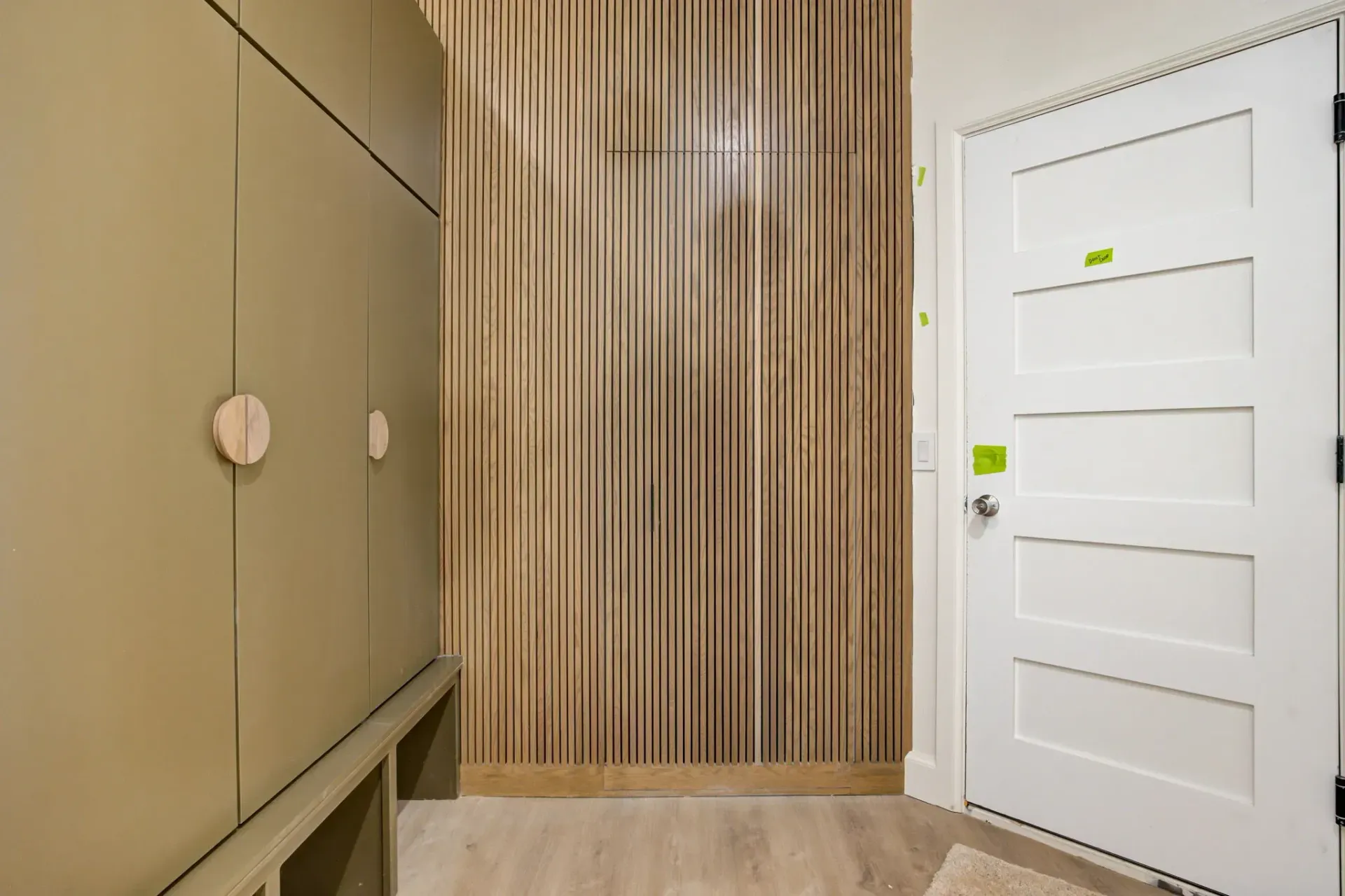 Modern hallway with beige cabinets, wood slat wall, and a white door with taped notes