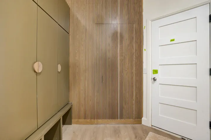Modern hallway with beige cabinets, wood slat wall, and a white door with taped notes