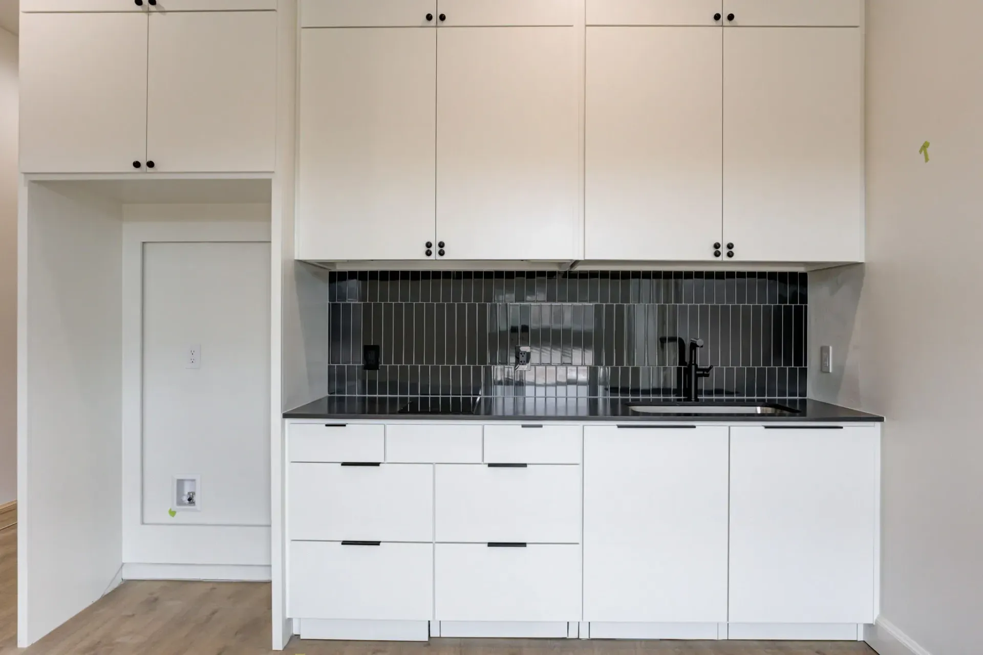 White kitchen with built-in cabinets, black backsplash, and open alcove on the left.