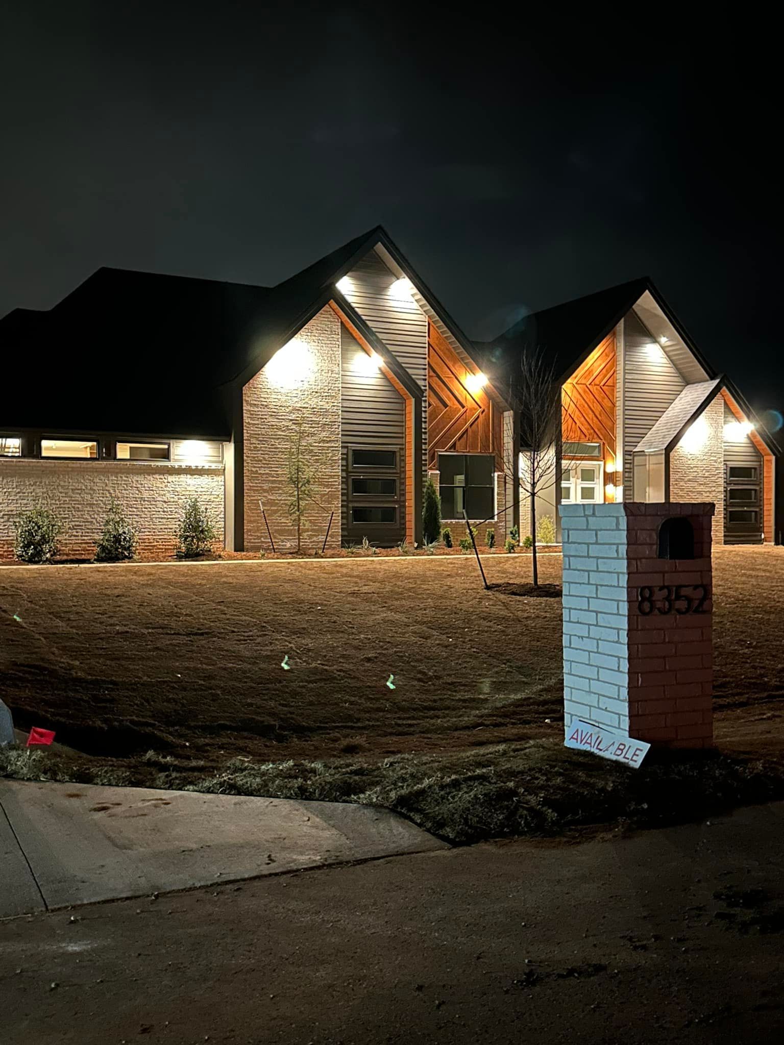 Night view of a modern stone house with warm exterior lights and a brick mailbox in front
