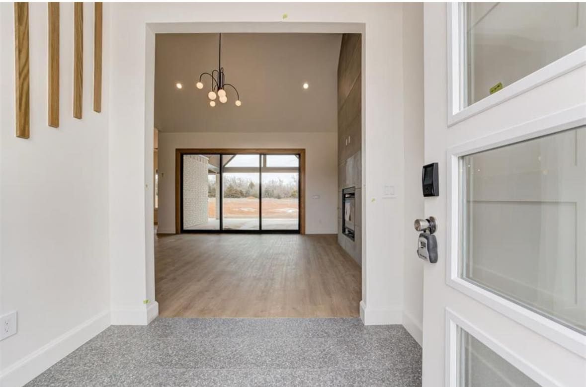 Modern entryway with white walls, gray carpet, wood floors, and large windows leading to a bright living room.