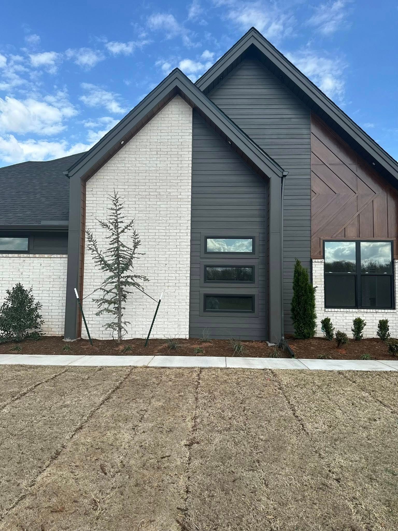 Modern house exterior with gray siding, white brick, and a gravel front yard under a blue sky