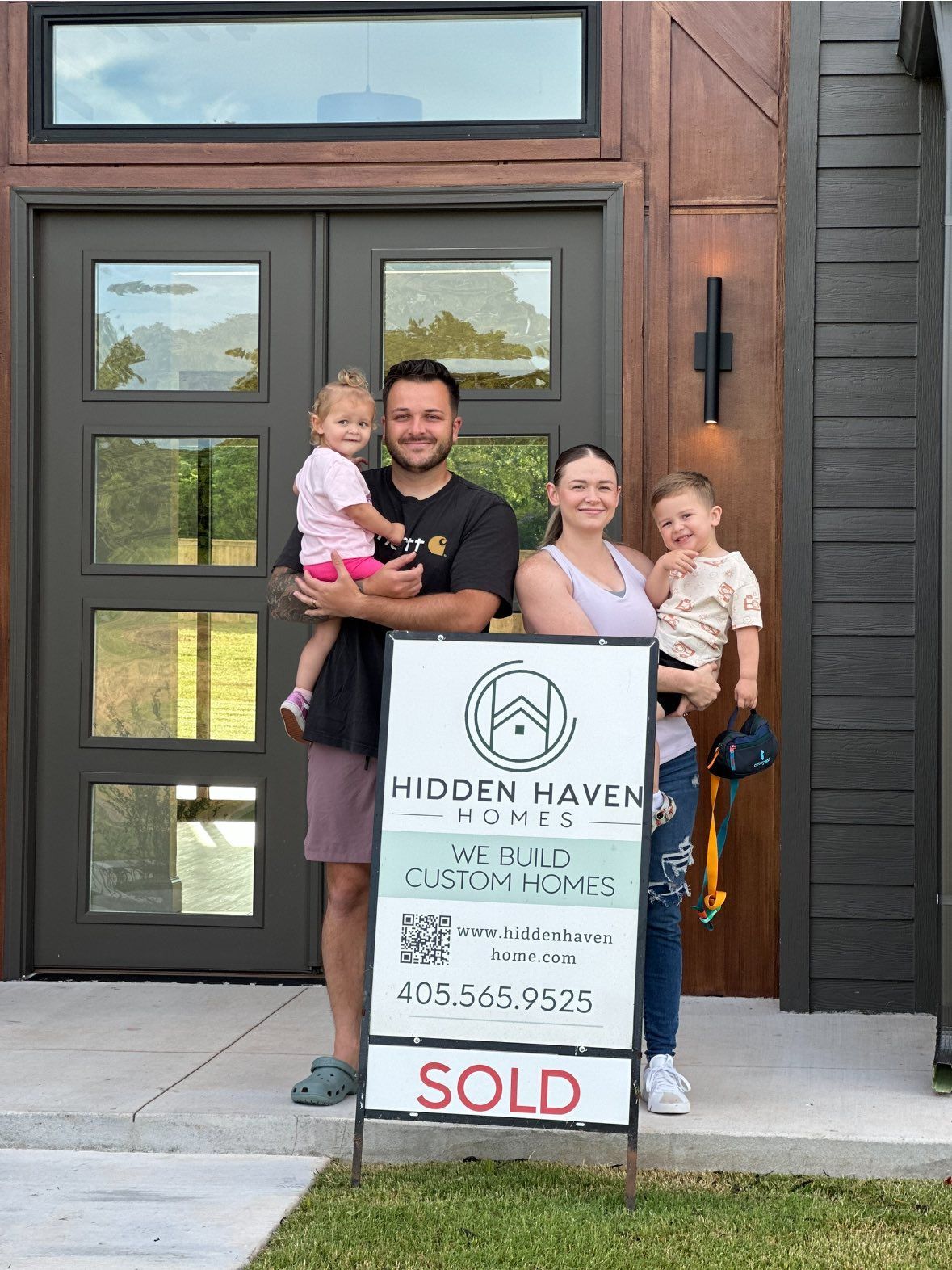Family standing outside a house with a real estate sign that says “SOLD”
