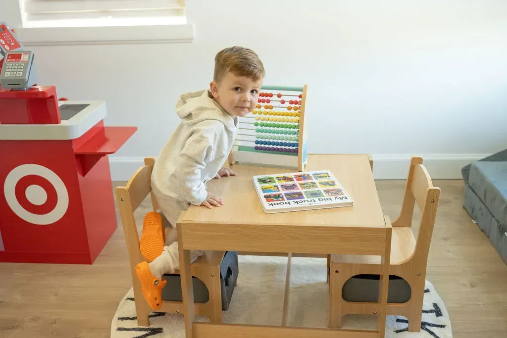 Child standing by a small wooden table with colorful abacus toys in a bright playroom
