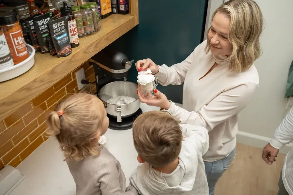 Woman shows children a food mixer in a kitchen counter area.