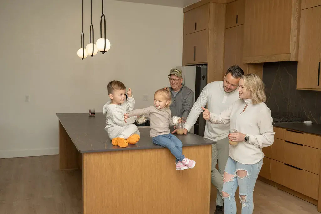 Family gathered in a modern kitchen, standing and sitting around a wooden island.