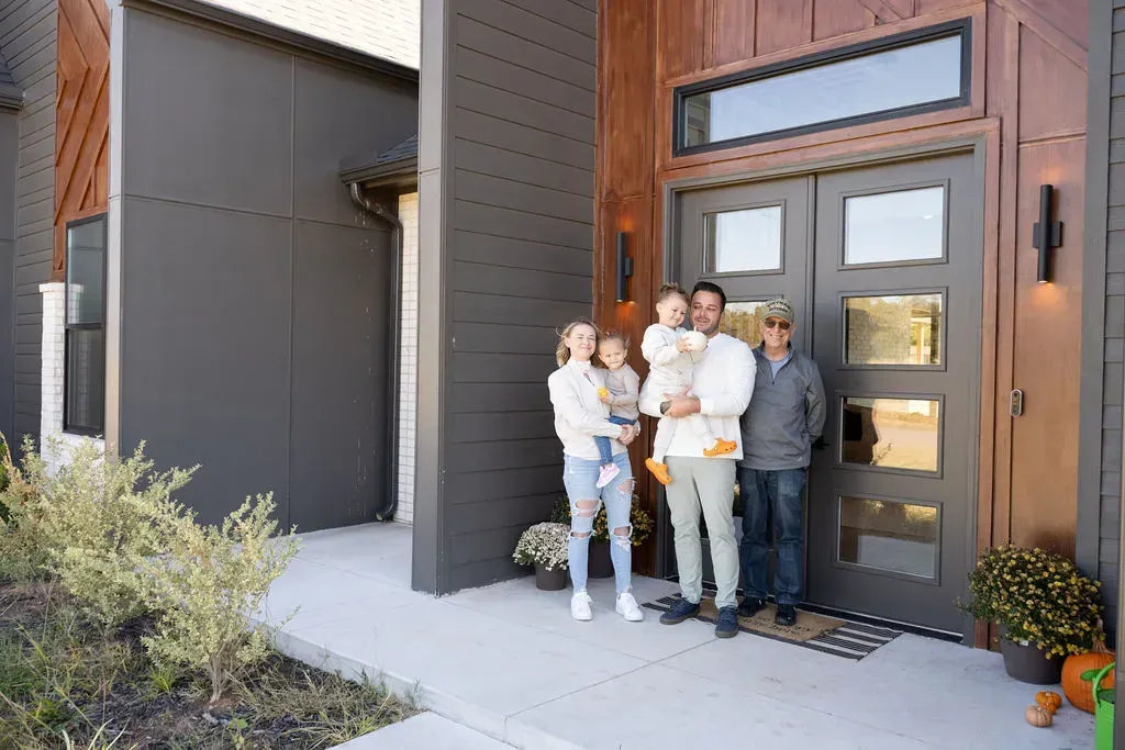 Four people standing at a home’s front door, posing outside a modern house
