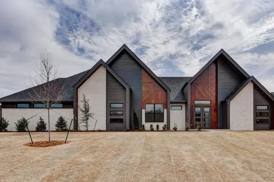 Modern house exterior with steep gables, mixed wood and white siding, and a wide gravel driveway