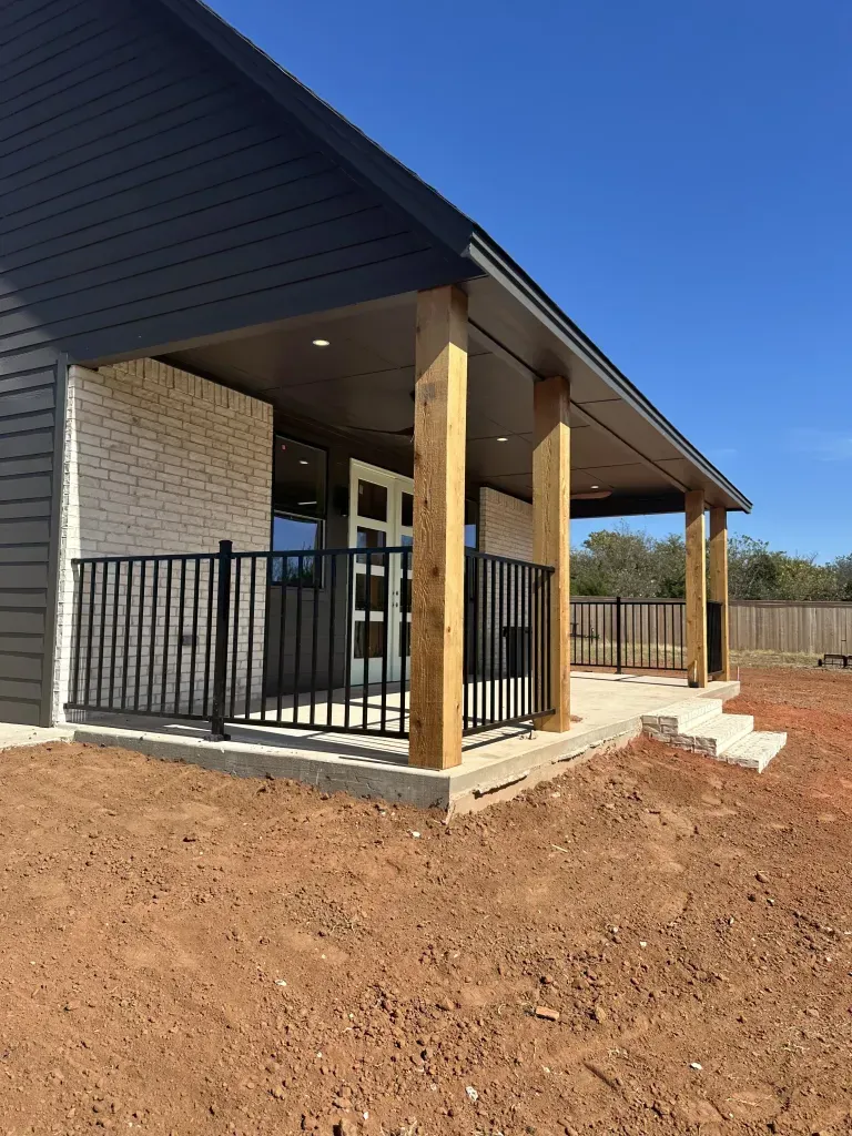 Modern house porch with black railings, wood posts, and red dirt yard under construction