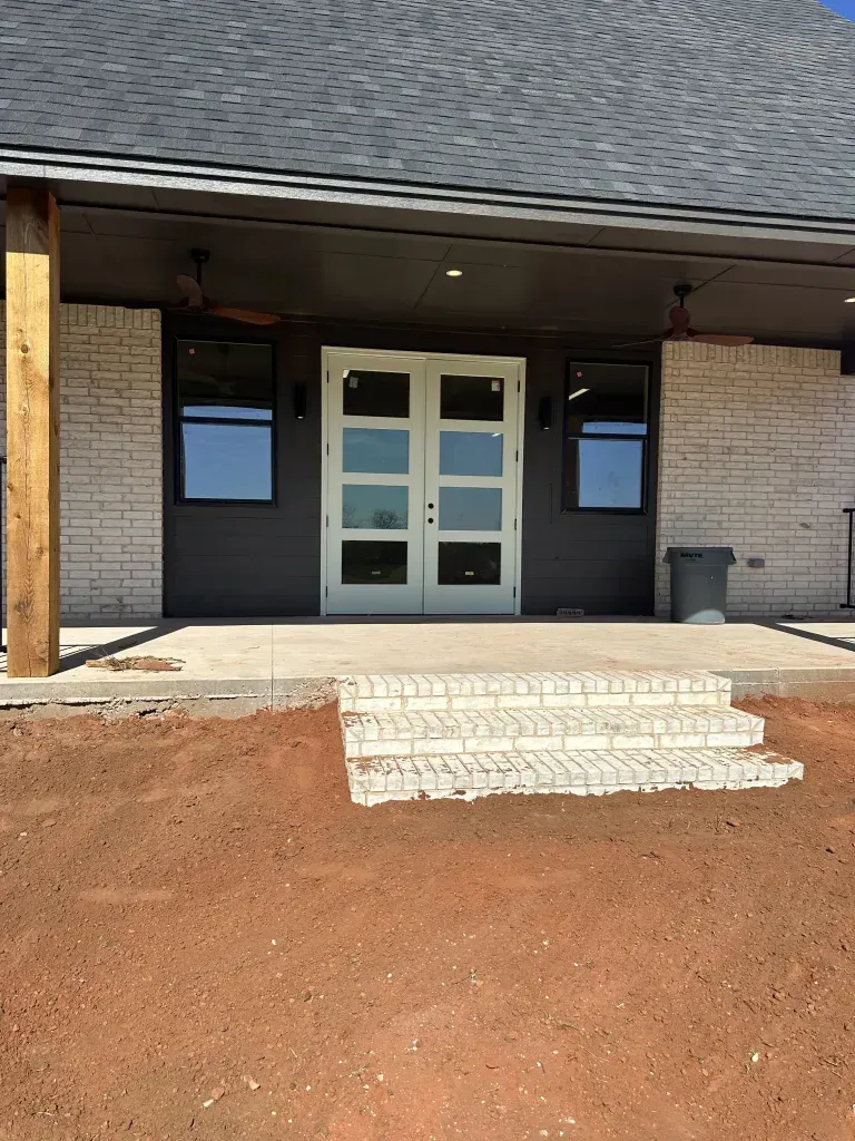 Building entrance with white double doors, dark trim, and a small concrete step in front of a dirt slope.