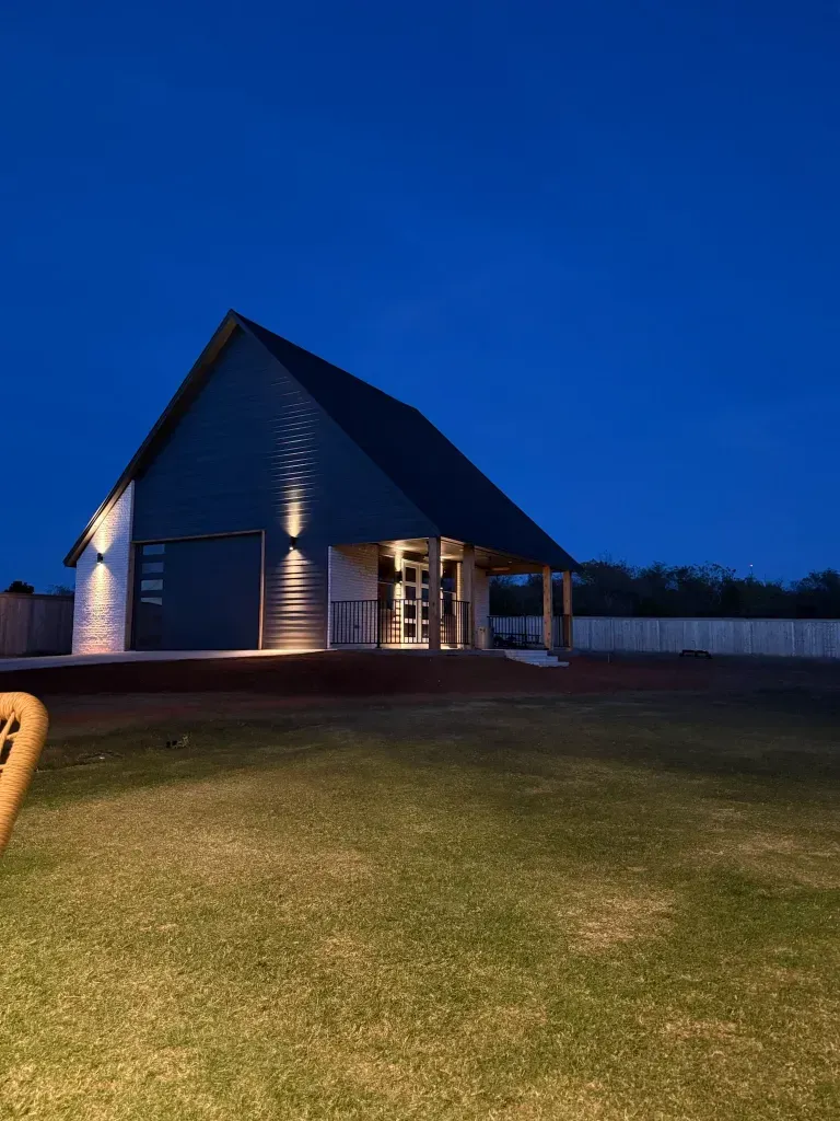 Modern dark building with a steep triangular roof, lit at night against a deep blue sky.