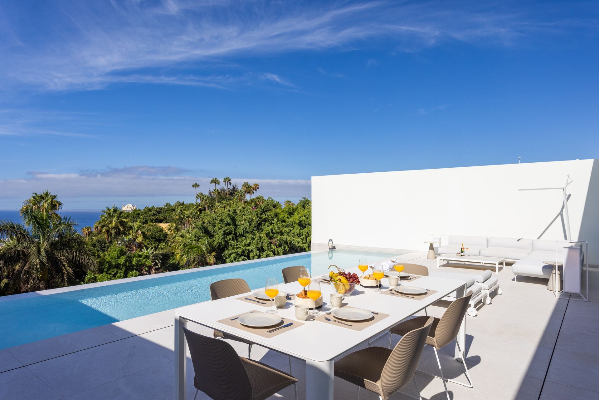 Rooftop dining terrace with white table, chairs, and an infinity pool overlooking the ocean
