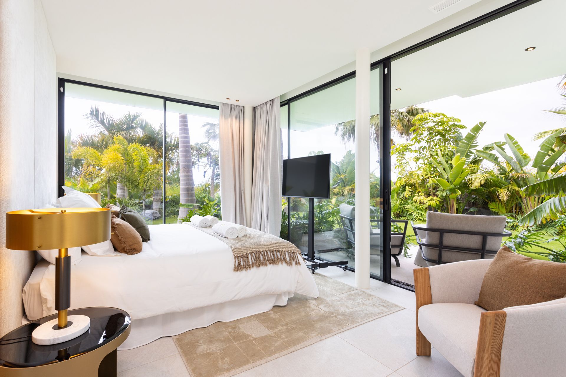 Bright modern bedroom with large glass doors, tropical garden view, and white bedding