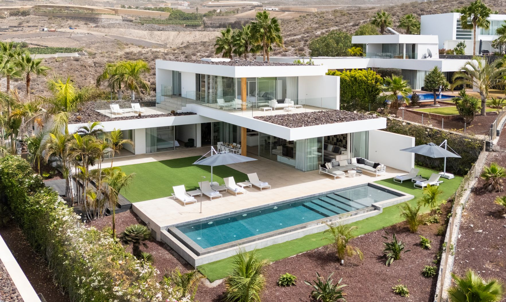 Modern white luxury villa with a turquoise pool and patio overlooking a desert landscape
