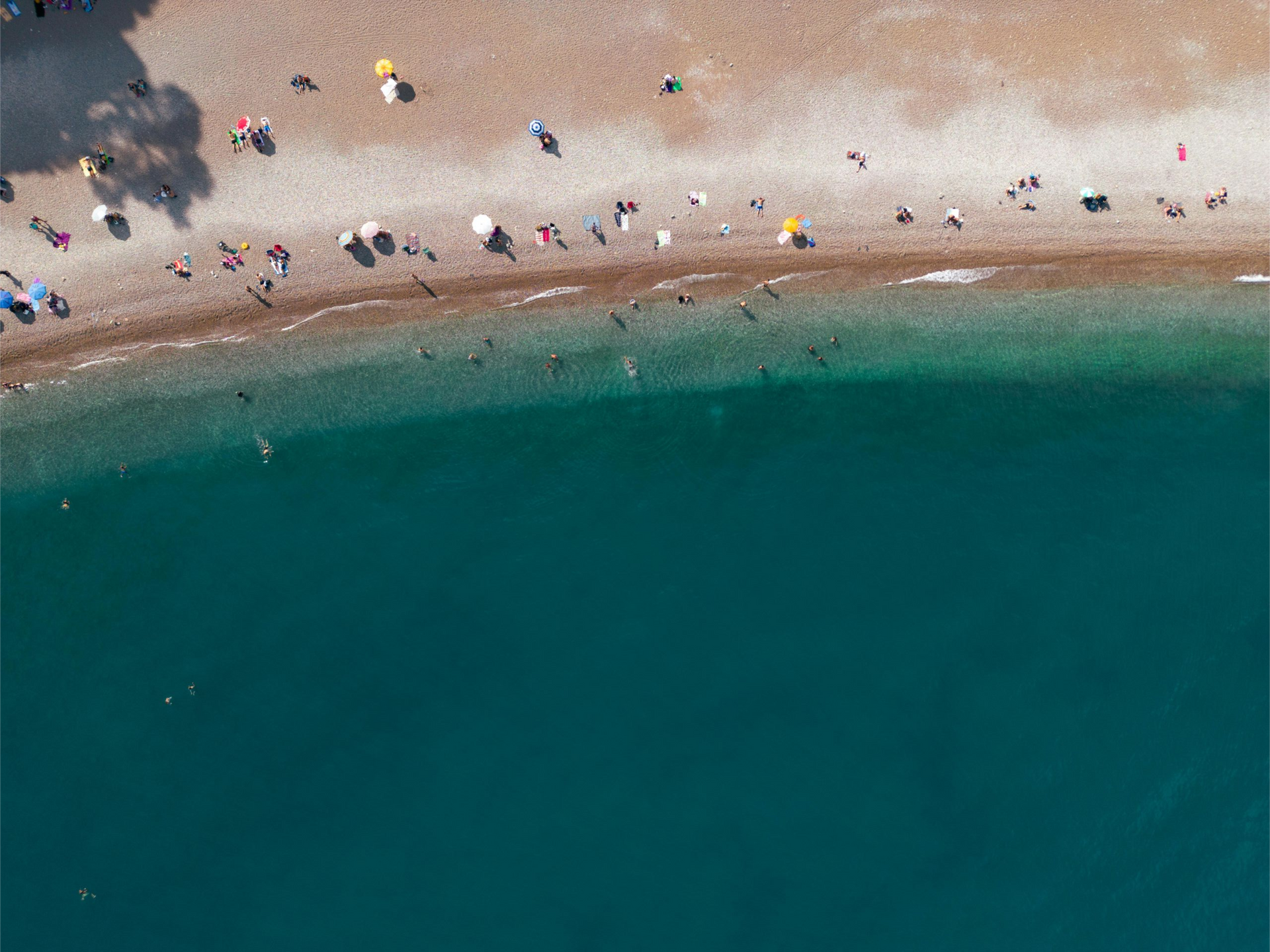 Aerial view of a sandy beach with scattered people beside clear turquoise water