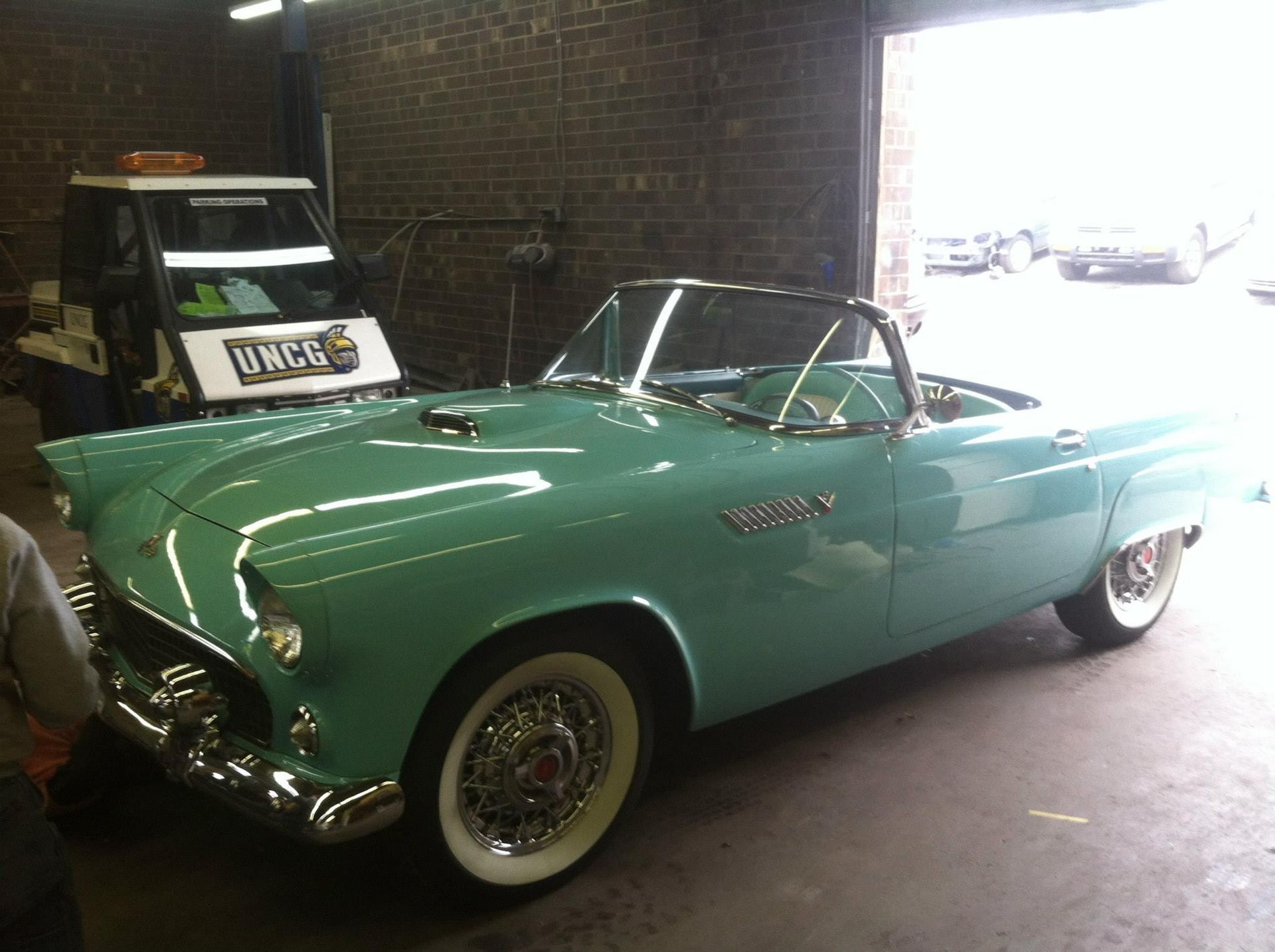 Turquoise vintage Ford Thunderbird convertible parked in a garage.